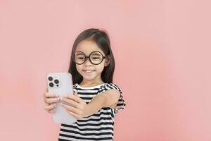 weinig meisje Speel telefoon mobiel. geïsoleerd Aan roze achtergrond foto