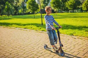 weinig jongen rijden een scooter in de park foto