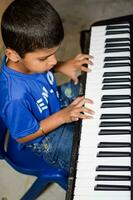 Aziatisch jongen spelen de synthesizer of piano. schattig weinig kind aan het leren hoe naar Speel piano. kind handen Aan de toetsenbord binnen. foto