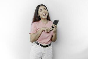een portret van een gelukkig Aziatisch vrouw is vervelend roze t-shirt en Holding haar telefoon, geïsoleerd door wit achtergrond foto