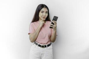 een attent jong vrouw vervelend roze t-shirt, Holding haar kin en haar telefoon geïsoleerd door wit achtergrond foto
