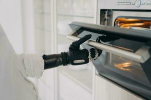 robotachtige cyberhand van gehandicapte persoon opent de oven in de keuken en gaat bakken. foto