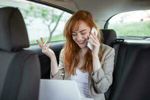 zakenvrouw pratend Aan de mobiel telefoon en gebruik makend van de laptop in de auto foto