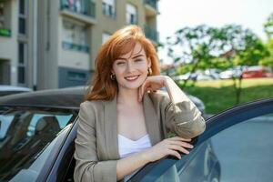 portret van gelukkig vrouw staand door auto Aan de straat. jong mooi caucasain vrouw staand achter een auto met geopend deur foto