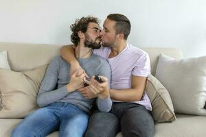 jong homoseksueel paar ontspannende Aan sofa in de leven kamer, omarmen en genieten van terwijl aan het kijken TV foto