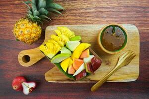 gesneden fruit salade, in Indonesië bekend net zo rujak buah of lutis of veel. geserveerd met pittig bruin suiker saus en grond pinda's in een bord Aan hout achtergrond foto