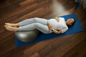 direct bovenstaand zwanger vrouw aan het doen prenataal gezond ontspanning opdrachten met een geschiktheid bal Aan een yoga mat Bij huis foto