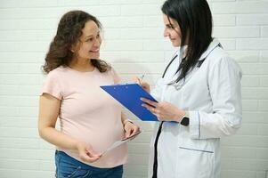 vrouw dokter gynaecoloog met klembord overleg plegen een gravid zwanger vrouw, voorschrijven geneesmiddelen. zwangerschap. 9 maand foto