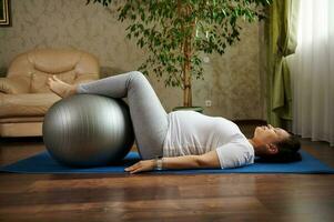 kant portret van een zwanger vrouw aan het doen prenataal gezond ontspanning opdrachten met een geschiktheid bal Aan een yoga mat Bij huis foto