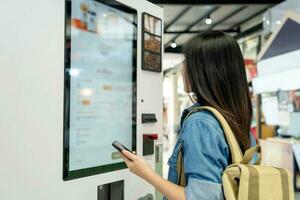 Aziatisch vrouw bestellen drinken van tintje scherm elektronisch machine in boodschappen doen winkelcentrum, elektronisch menu. foto