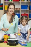 jong moeder spelen met zijn zes maanden oud baby meisje binnenshuis. mam onderwijs me hoe naar Speel de drums foto