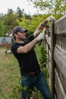 Mens bouwt secties van hek in de omgeving van zijn werf uit van planken - zomer huis klusjes in de achtertuin foto