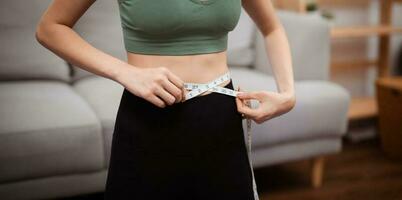 Aziatisch gezond vrouw dieet gewicht verlies. slank vrouw meten taille met meten plakband na eetpatroon Bij huis gewicht controle. foto