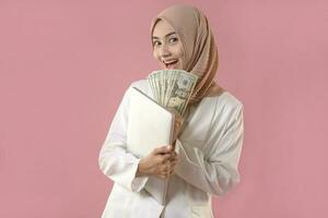 jong moslim vrouw houden geld en laptop Aan geïsoleerd achtergrond. foto