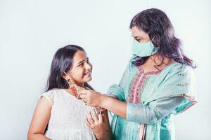 Indisch moeder zetten mooi handgemaakt gezicht masker Aan haar glimlachen dochter foto