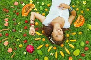 vrouw aan het liegen Aan een gras met de patroon van kleurrijk vers exotisch fruit in de omgeving van foto