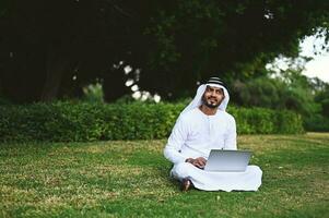 gelukkig Arabisch zakenman gebruik makend van laptop buitenshuis in een park foto