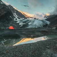 extreem camping. oranje versterkt tent tegen de achtergrond van een groot gletsjer Aan een grote hoogte plateau. bergbeklimmen kamp Bij de blauw meer met reflectie. actie. foto