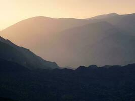 toneel- dageraad berg landschap met licht mist in vallei tussen bergen silhouetten onder bewolkt lucht. levendig zonsondergang of zonsopkomst landschap met laag wolken in berg vallei in zacht kleur. foto