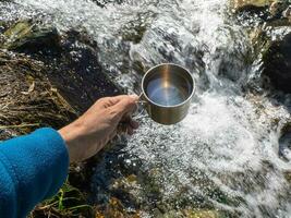 hand- Holding een wandelaars kop met schoon drinken water van een berg stroom. foto