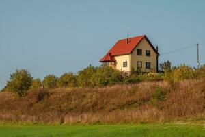 een modern geel huisje met een rood dak Aan een groen heuvel. foto