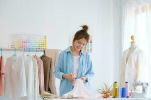een jong Aziatisch vrouw mode ontwerper is snijdend kleding stof en bereiden een patroon voor een nieuw verzameling. foto
