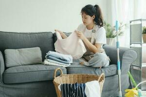 jong vrouw vouwen kleren Aan sofa Bij huis. foto