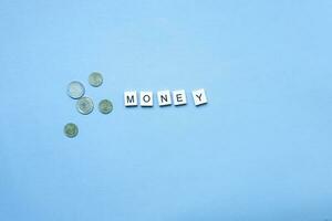 de woord geld van houten brieven. vlak leggen munten Aan blauw achtergrond foto