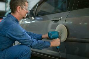 Kaukasisch Mens is gebruik makend van auto polijsten machine in reparatie monteur schilderij winkel foto