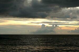 een bewolkt lucht over- de oceaan met een donker lucht en de zon instelling achter het foto