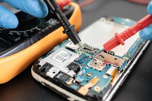 technicus reparatie binnenkant van mobiele telefoon door soldeerbout geïntegreerde schakeling foto