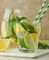 limonade in een transparant glas met citroen, limoen, rozemarijn takjes en munt bladeren Aan een wit achtergrond foto