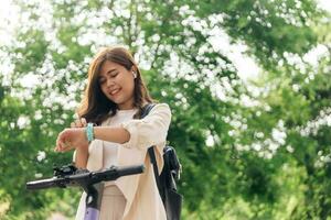 gelukkig jong Aziatisch vrouw in oortelefoons op zoek Bij polshorloge terwijl rijden fiets in park foto