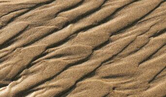 zand strand structuur achtergrond in zomer, top visie bruin zanderig ruw oppervlakte met Golf rimpeling van zee water met kopiëren ruimte voor zomer banier ontwerp, natuurlijk zand steen door de zee foto