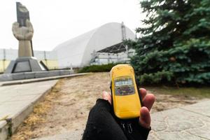 Oekraïne 2019- persoonshand met vingerloze handschoenen toont stralingsniveaus op dosimeter met kerncentrale op de achtergrond foto