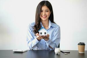 Aziatisch vrouw met lang haar- in blauw overhemd genieten van besparing geld voor huis aankoop door varkentje bank spaargeld concept. foto