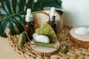 jade gua sha schraper en rol gezicht massager, flessen van kunstmatig serum voor de gezicht Aan houten staat. foto