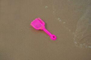 roze speelgoed- plastic Schep Aan strand zand en golven. concept foto voor zomer tijd