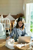 Aziatisch bedrijf vrouw Holding pen en gebruik makend van laptop werken Aan bureau in de cafe. bedrijf vrouw werk en Speel met wit kat Aan de tafel. foto