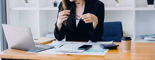 Aziatisch bedrijf vrouw gebruik makend van rekenmachine en laptop voor aan het doen wiskunde financiën Aan een kantoor bureau, belasting, rapport, boekhouding, statistieken, en analytisch Onderzoek concept foto