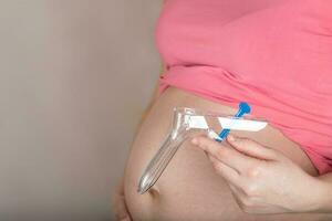 jong zwanger vrouw houdt beschikbaar vaginaal speculum dichtbij naar haar buik. foto