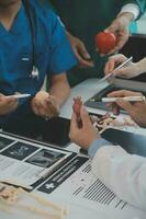 multiraciaal medisch team hebben een vergadering met artsen in wit laboratorium jassen en chirurgisch scrubs gezeten Bij een tafel bespreken een patiënten records foto