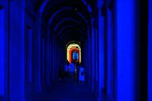 Bologna, Italië- juni 23, 2023-mensen wandeling Bij nacht onder de arcades leidend naar de heiligdom van san luca verlichte voor de eerste editie van de bologna arcades festival. foto