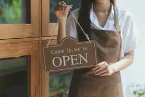 Welkom. open. barista, serveerster vrouw draaien Open teken bord Aan glas deur in modern cafe koffie winkel klaar naar onderhoud, cafe restaurant, kleinhandel op te slaan, klein bedrijf baasje, voedsel en drinken concept foto