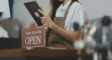 Welkom. open. barista, serveerster vrouw draaien Open teken bord Aan glas deur in modern cafe koffie winkel klaar naar onderhoud, cafe restaurant, kleinhandel op te slaan, klein bedrijf baasje, voedsel en drinken concept foto