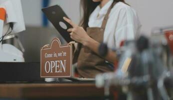 Welkom. open. barista, serveerster vrouw draaien Open teken bord Aan glas deur in modern cafe koffie winkel klaar naar onderhoud, cafe restaurant, kleinhandel op te slaan, klein bedrijf baasje, voedsel en drinken concept foto