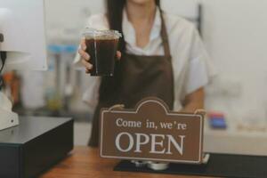 Welkom. open. barista, serveerster vrouw draaien Open teken bord Aan glas deur in modern cafe koffie winkel klaar naar onderhoud, cafe restaurant, kleinhandel op te slaan, klein bedrijf baasje, voedsel en drinken concept foto