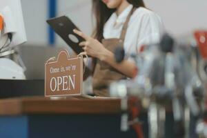 Welkom. open. barista, serveerster vrouw draaien Open teken bord Aan glas deur in modern cafe koffie winkel klaar naar onderhoud, cafe restaurant, kleinhandel op te slaan, klein bedrijf baasje, voedsel en drinken concept foto