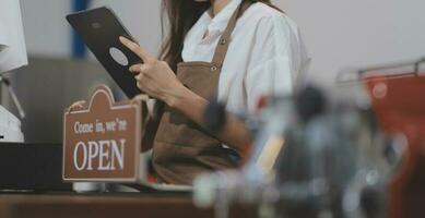 Welkom. open. barista, serveerster vrouw draaien Open teken bord Aan glas deur in modern cafe koffie winkel klaar naar onderhoud, cafe restaurant, kleinhandel op te slaan, klein bedrijf baasje, voedsel en drinken concept foto