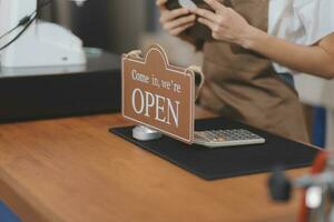 Welkom. open. barista, serveerster vrouw draaien Open teken bord Aan glas deur in modern cafe koffie winkel klaar naar onderhoud, cafe restaurant, kleinhandel op te slaan, klein bedrijf baasje, voedsel en drinken concept foto